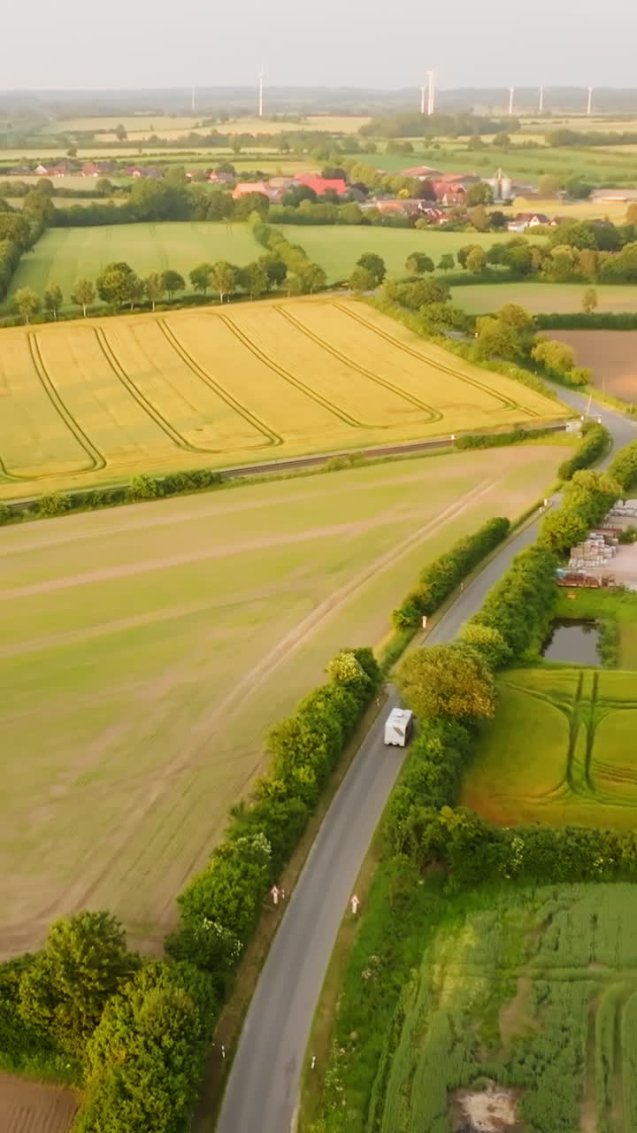 Vertical aerial of a camper van driving on the countryside, wind turbine backdrop