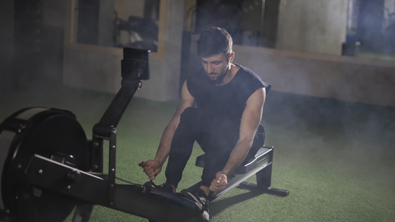 Handsome athlete works out in gym with rowing machine