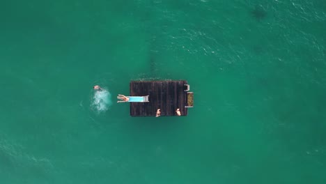 Aerial-top-down-shot-of-kids-having-fun-on-floating-platform-sliding-on-water-chute-into-ocean