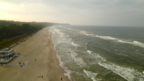 Asombrosos-Y-Sombríos-Drones-Al-Atardecer-Nublados-Vuelan-Sobre-Las-Olas-Rompiendo-Contra-La-Playa-De-Arena,-Antena,-Wladyslawowo,-Polonia