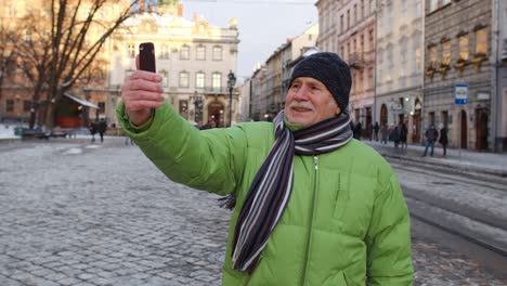 Senior-man-tourist-taking-selfie,-making-online-video-call-with-smart-phone-in-winter-city-center