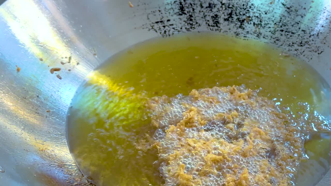 Close-up of food frying in hot oil, showcasing bubbling and sizzling in a metallic pan.