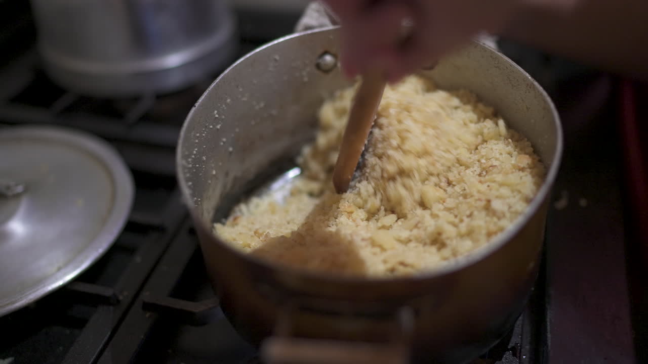 Reviro cooks on stovetop as a hand stirs the crumbly mixture of flour and fat in a pan, showing texture and movement in the early stages of this rustic South American dish — cooking action close-up.