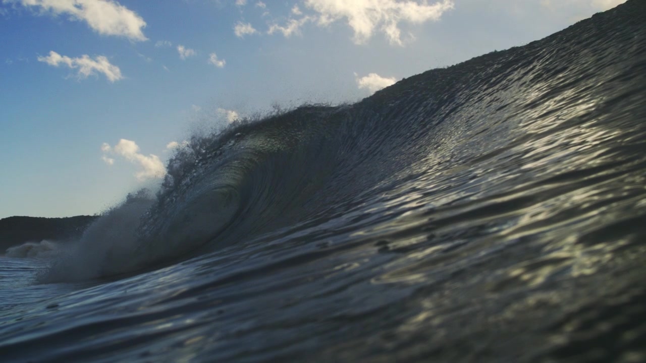 Curling ocean wave breaking near the water surface beneath blue sky in smooth slow motion