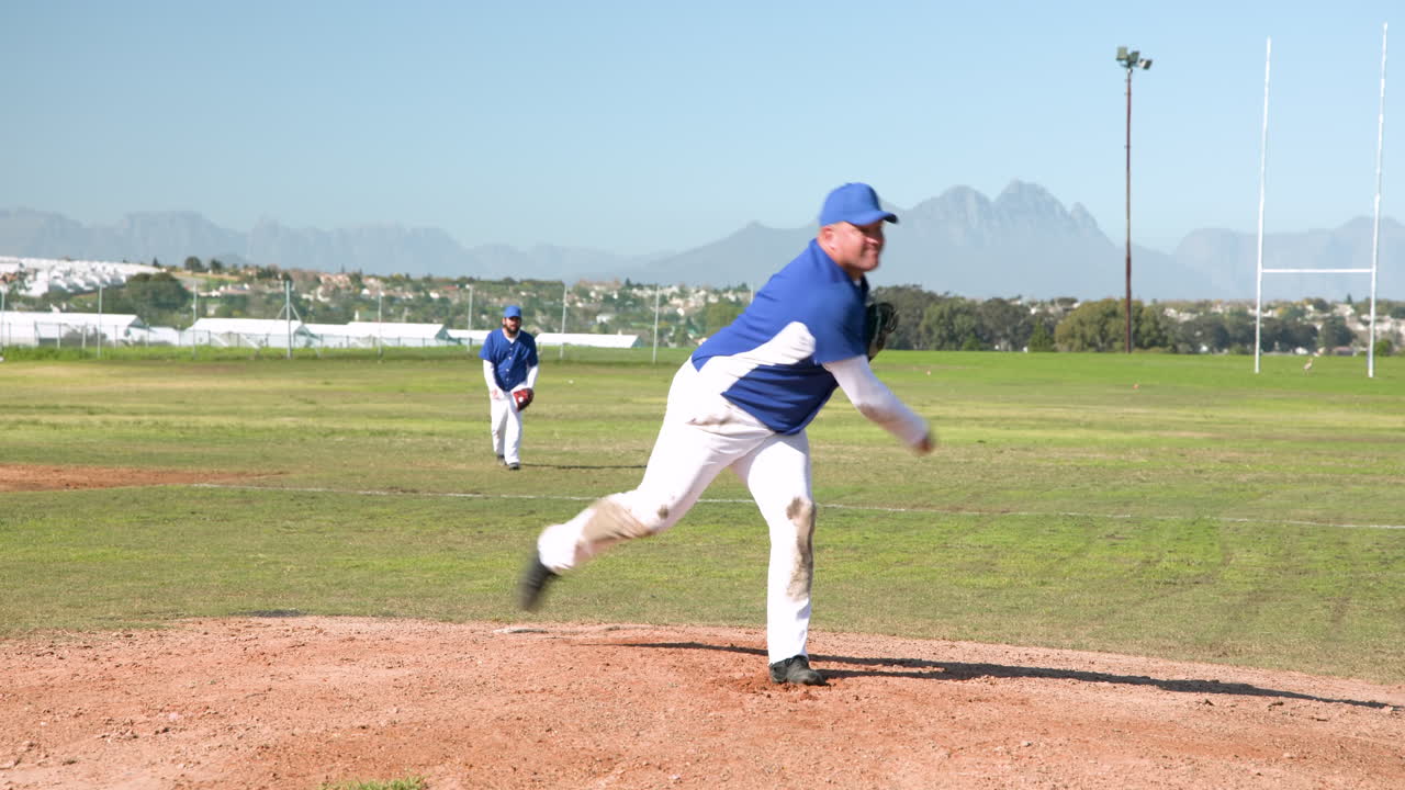 Lancio sul campo da baseball, uomo in uniforme blu con guanto, compagno di squadra che osserva.
