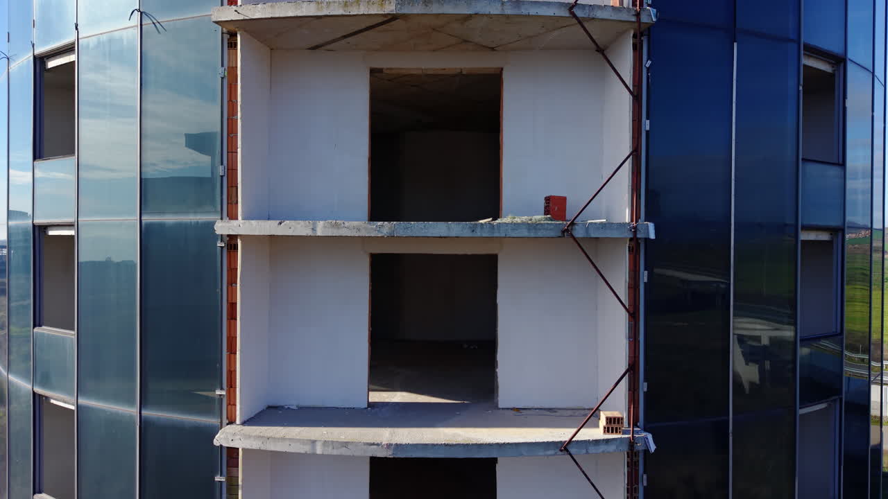 Primo piano di un edificio rotondo in costruzione con pannelli mancanti e interni a vista. Sfondo rurale. Edificio cilindrico con facciata in vetro e mattoni