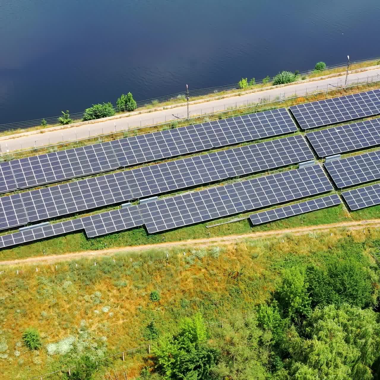Flight over long solar panels on field. Photovoltaic solar cells near the road at bright sunny day. Alternative green energy. Aerial view