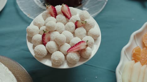 white coconut truffles arranged on a plate with fresh strawberry slices on blue table setting