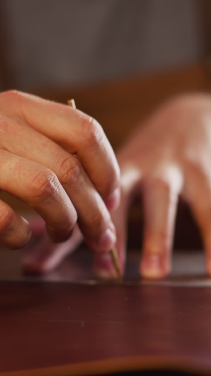 Leathersmith draws outline on leather sheet with plastic mould at workplace in home studio closeup. Master makes item of natural material. Art hobby