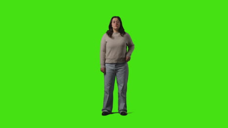 full length shot of serious casually dressed young woman standing against green screen with hands in pockets