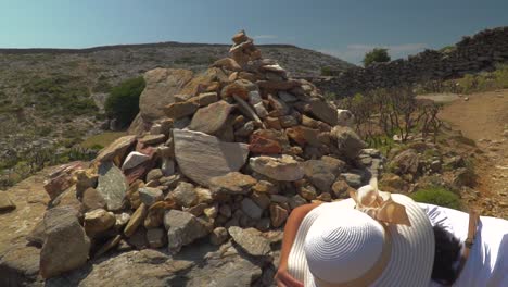 Female-in-summer-hiking-outfir-putting-stone-on-pile,-also-known-as-cairn,-in-arrid-landscape-SLOW-MOTION