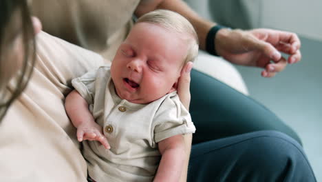 infant boy falling asleep in mother's hands. mom waving her newborn who's yawning. close up.