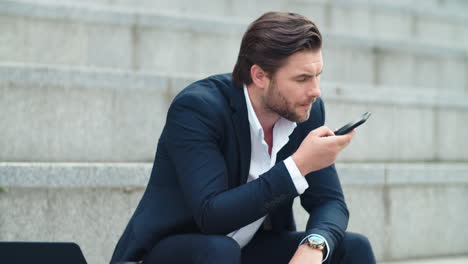 homme d'affaires confiant enregistrant un message audio sur un smartphone dans la rue