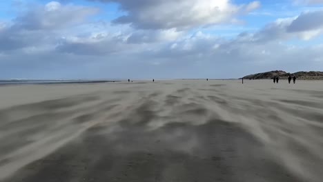 Storm-on-the-coast,-people-walk-on-the-beach-through-the-shifting-sand