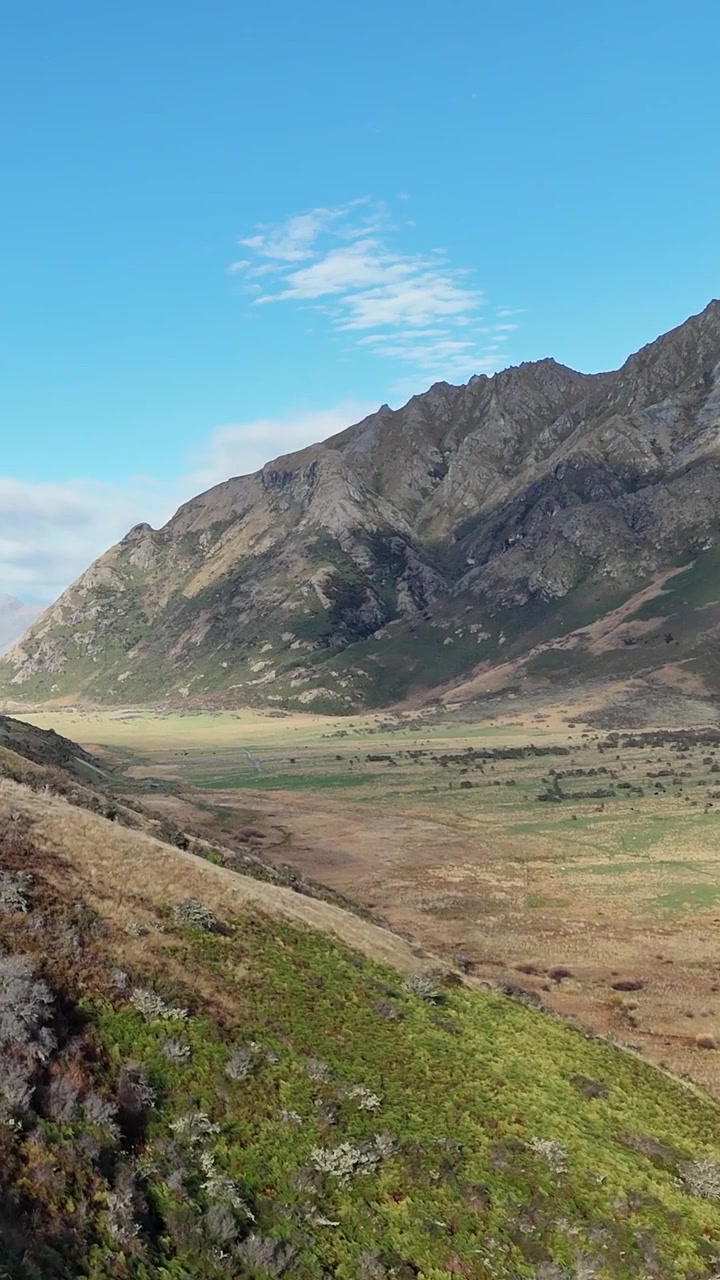 Filmato cinematografico con drone che mostra una strada tortuosa attraverso colline verdi e lussureggianti e aspre cime montuose.