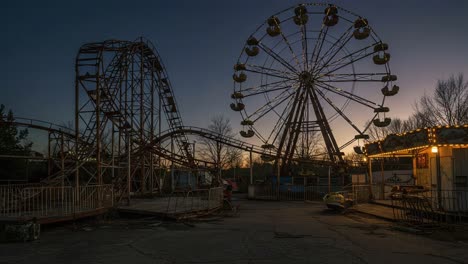 Abandoned Amusement Park at Dusk: A Hauntingly Beautiful Scene of Rusting Rides, Setting Sun, and Lush Yet Neglected Nature Surrounding the Ferris Wheel and Roller Coaster