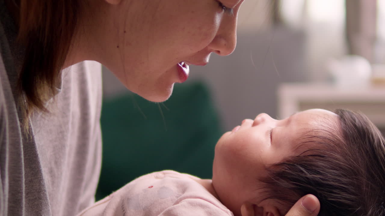 Singing a sweet lullaby to her sleeping newborn child, a mother wakes her baby from its sleep.