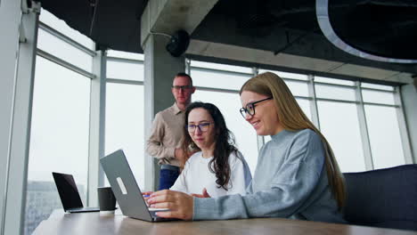 happy positive people laugh looking at laptop. male colleague comes up standing behind the ladies. low angle view.