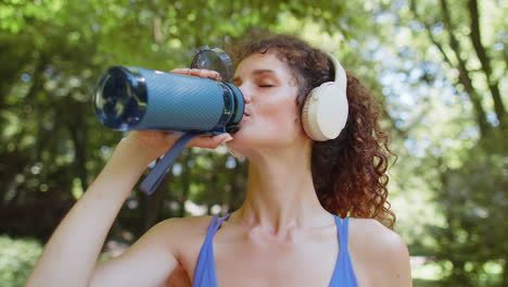 athletic fit sport runner girl drinking water from bottle after training workout cardio in park