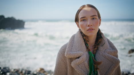 serene woman posing coastline in winter coat closeup. reflective stylish lady