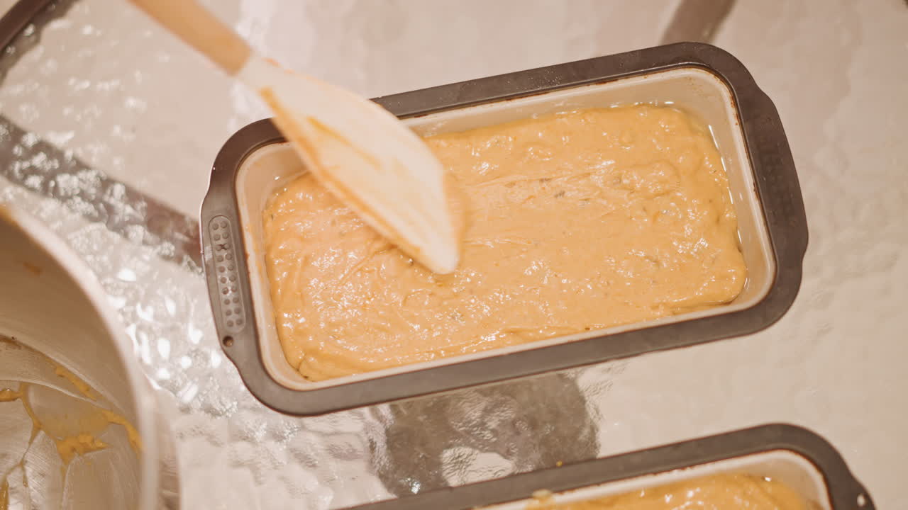 Pumpkin batter in loaf pan, wooden spatula smoothing spiced batter, metal mixing bowl at side, granulated sugar sparkle on surface, warm golden light, cozy kitchen atmosphere, preparing pumpkin