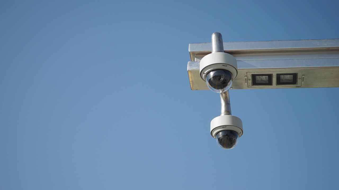 Two security cameras mounted on a metal pole against a clear blue sky.