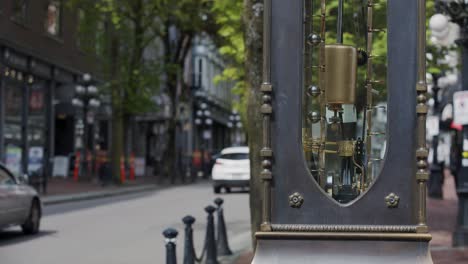 close up of famous gastown steam clock pendulum moving, cars driving in background, vancouver, british columbia, canada