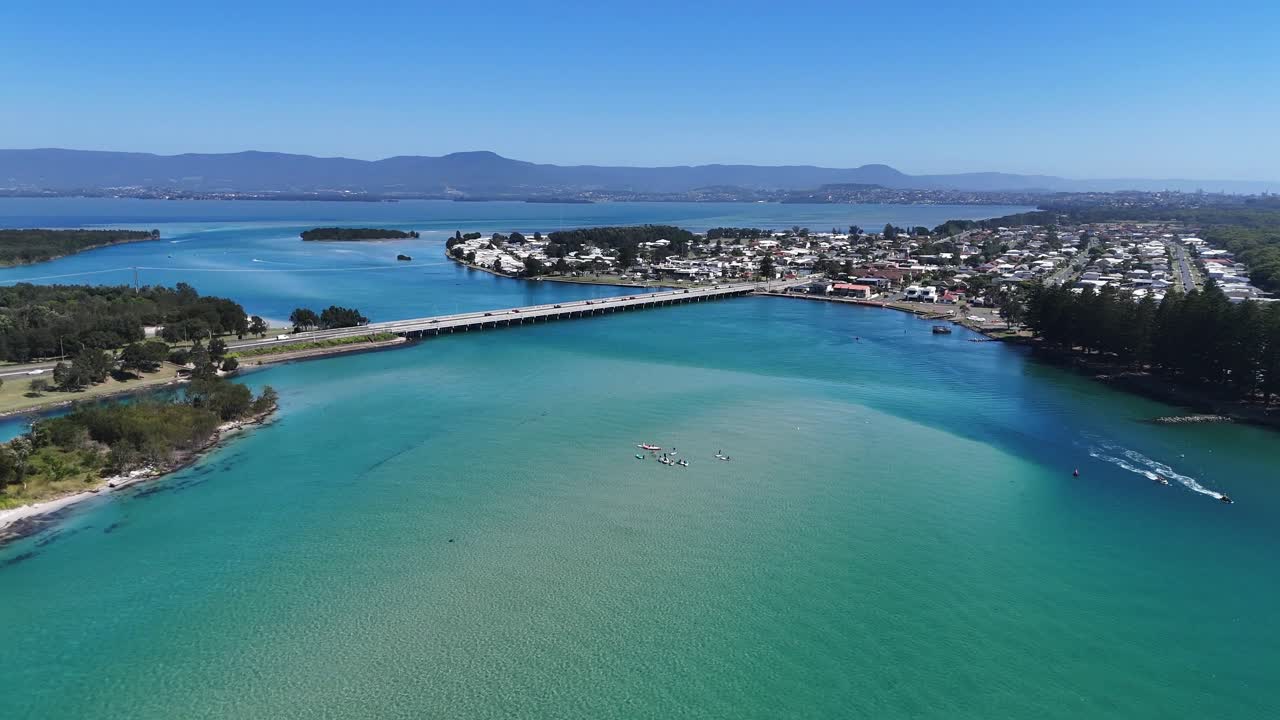 Fluido passaggio di drone sopra le acque calme dell'insenatura, incorniciate da banchi di sabbia e sviluppo costiero, auto che attraversano il ponte, dolly aereo