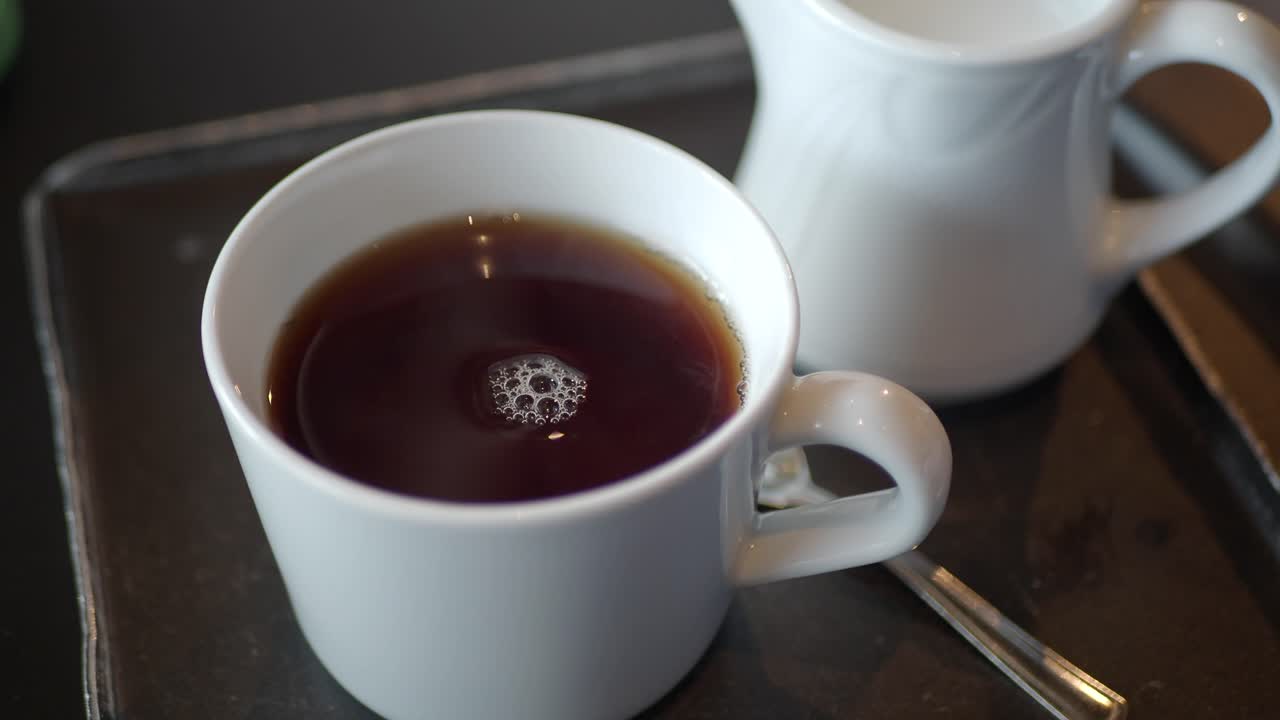 Close-up of a cup of hot tea with a creamer on a tray