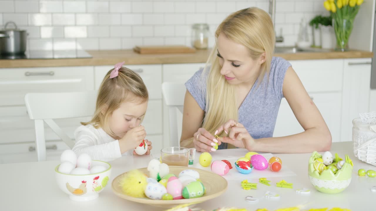 Mother looking at girl coloring eggs