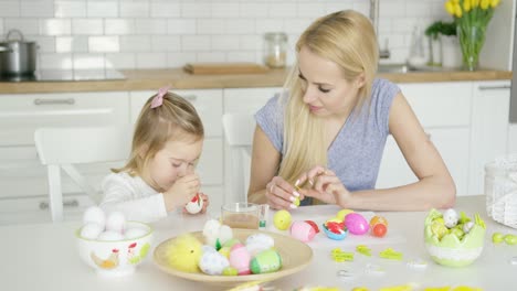 mother looking at girl coloring eggs