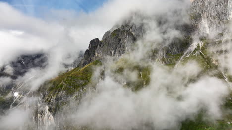 beautiful slow moving drone shot of rocky mountain side in austrian alps through misty clouds