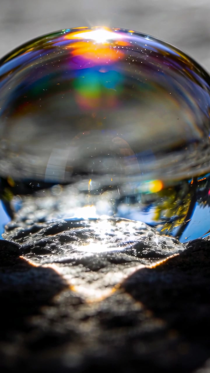 Vertical video: Sunlight striking soap bubble creating shimmer on wet rock, reflecting inverted sky