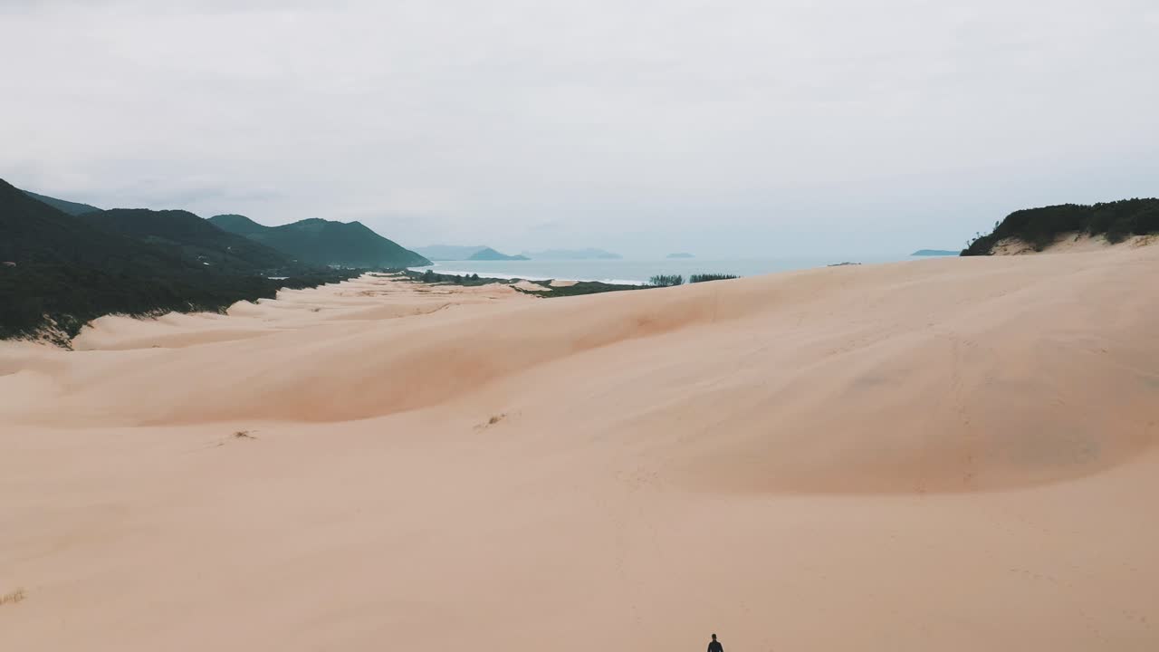establecimiento de tiro de sandboarder caminando sobre dunas de arena en la playa de garopaba, santa catarina, brasil