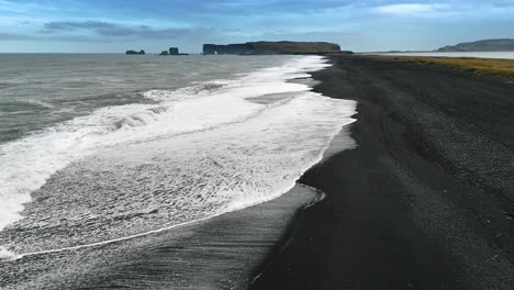 sea waves splashing on the beach with black sand. silhouettes of steep rocks at backdrop. iceland wilderness.