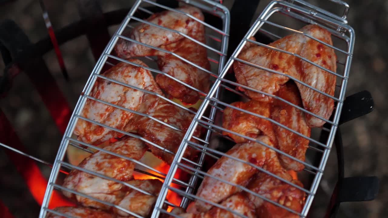 Handheld slow motion shot of spicy marinated chicken wings sizzling over fire.