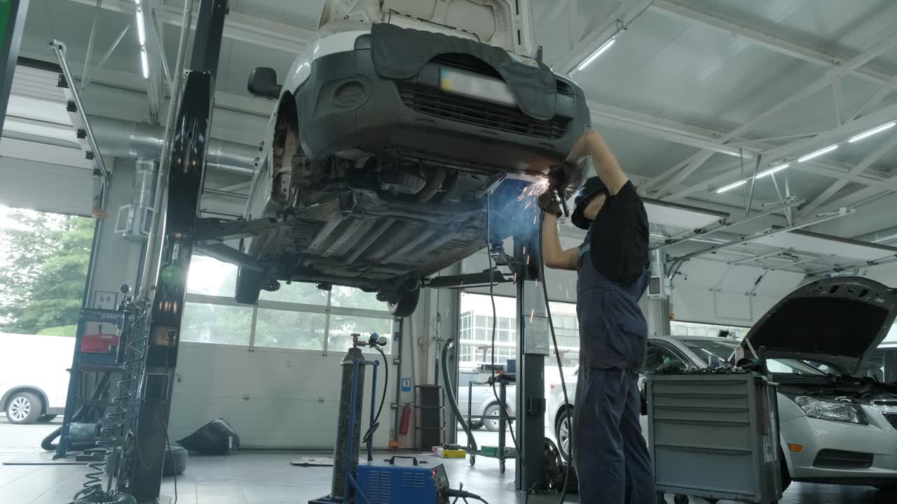 자동차 서비스 노동자는 자동차의 배기가스 파이프를 용접하고 수리합니다. 들어올린 차에 대한 근접 용접 작업. 뒤에서 볼 때. 기계공은 차의 바닥을 용접합니다.
