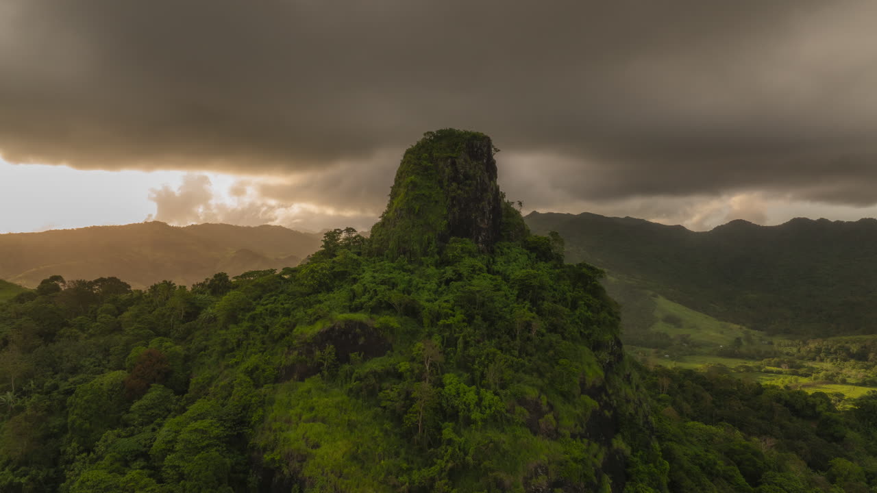 Drone hyperlapse at sunset over a rocky peak on Viti Levu, Fiji. Forward aerial shot with rainforest, mountains, and dramatic golden light