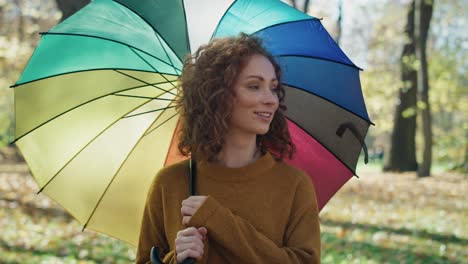 mujer caucásica con un paraguas colorido caminando en el parque de otoño.