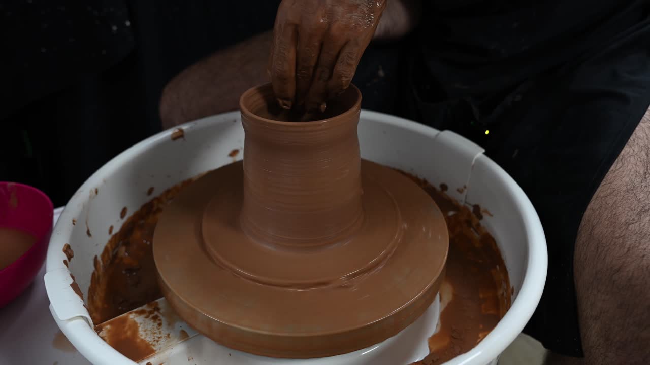 En mandlig pottemager bruger en drejeskive til at demonstrere den grundlæggende teknik til at forme en ler cylinder, traditionelt keramisk håndværk