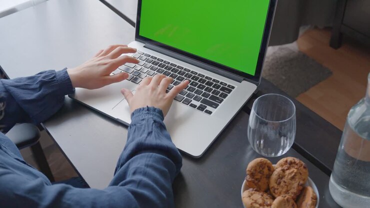 Aufnahme über die Schulter einer Frau, die an einem Laptop mit einem grünen Bildschirm tippt.
