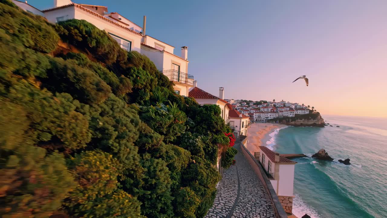 Aerial video captures a scenic coastal village at sunset, showcasing stone houses and a winding