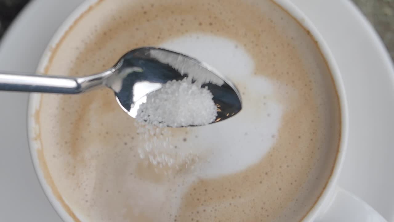 A spoon of sugar about to be added to a cup of coffee.
