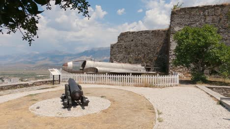 Exhibición-De-Fuselaje-Oxidado-De-Cañón-Viejo-Y-Avión-En-El-Castillo-De-Gjirokaster,-Tiro-Panorámico