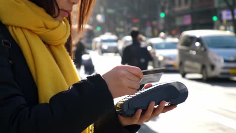 urban payment interaction: a woman using a payment terminal on a busy street while wearing a yellow scarf in bright daylight