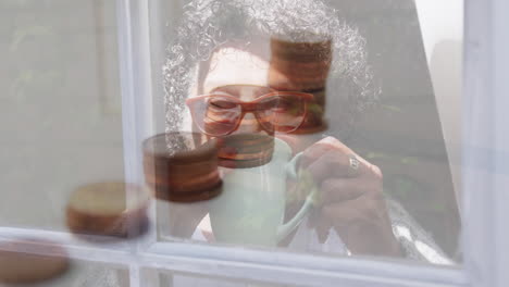 animation of stacks of coins over worried senior woman drinking tea at home