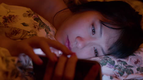 Close-up-on-lonely-asian-girl-with-insomnia-browsing-social-media-feed-on-the-phone-in-bed-at-night