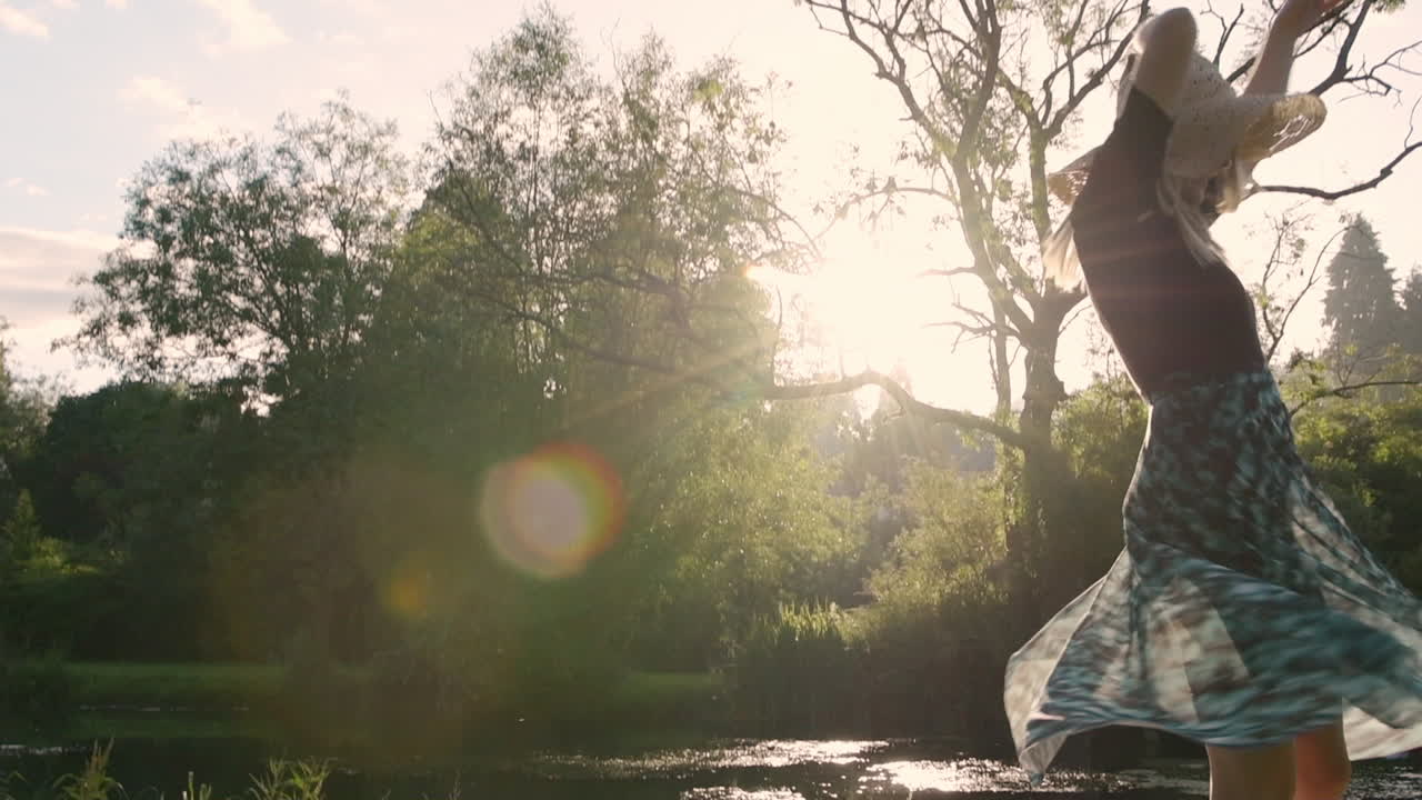 A Gorgeous Lady Wearing Picnic Hat Gracefully Spinning In The Park. Sunshine Flare In The Background - medium full shot - slow motion