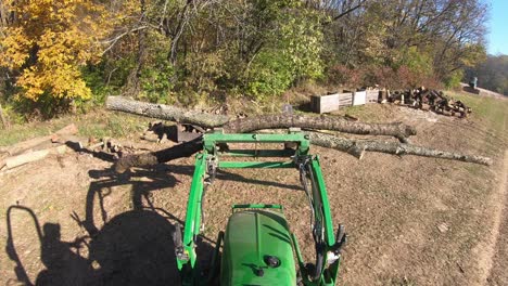 high angle point of view on small green tractor while using lift forks to move logs to be cut for a fireplace