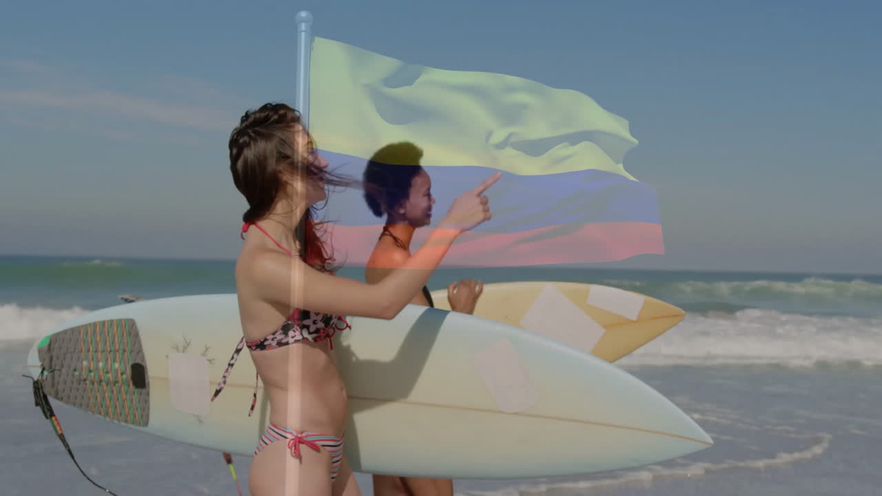 Two women with surfboards on beach, Colombian flag animation over scene